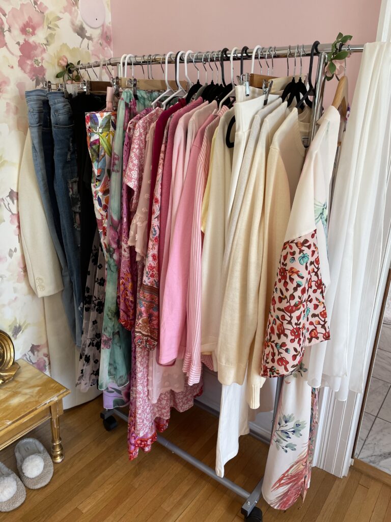 hanging rack with 33 pieces of clothing for Spring wardrobe in pinks, greens, and ivory